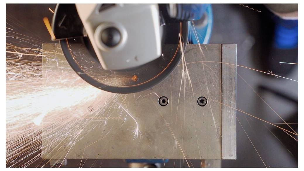 Eine Nahaufnahme einer Metallsäge, die Funken erzeugt, während sie ein Metallstück durchschneidet, was Industriearbeit und Präzision veranschaulicht.