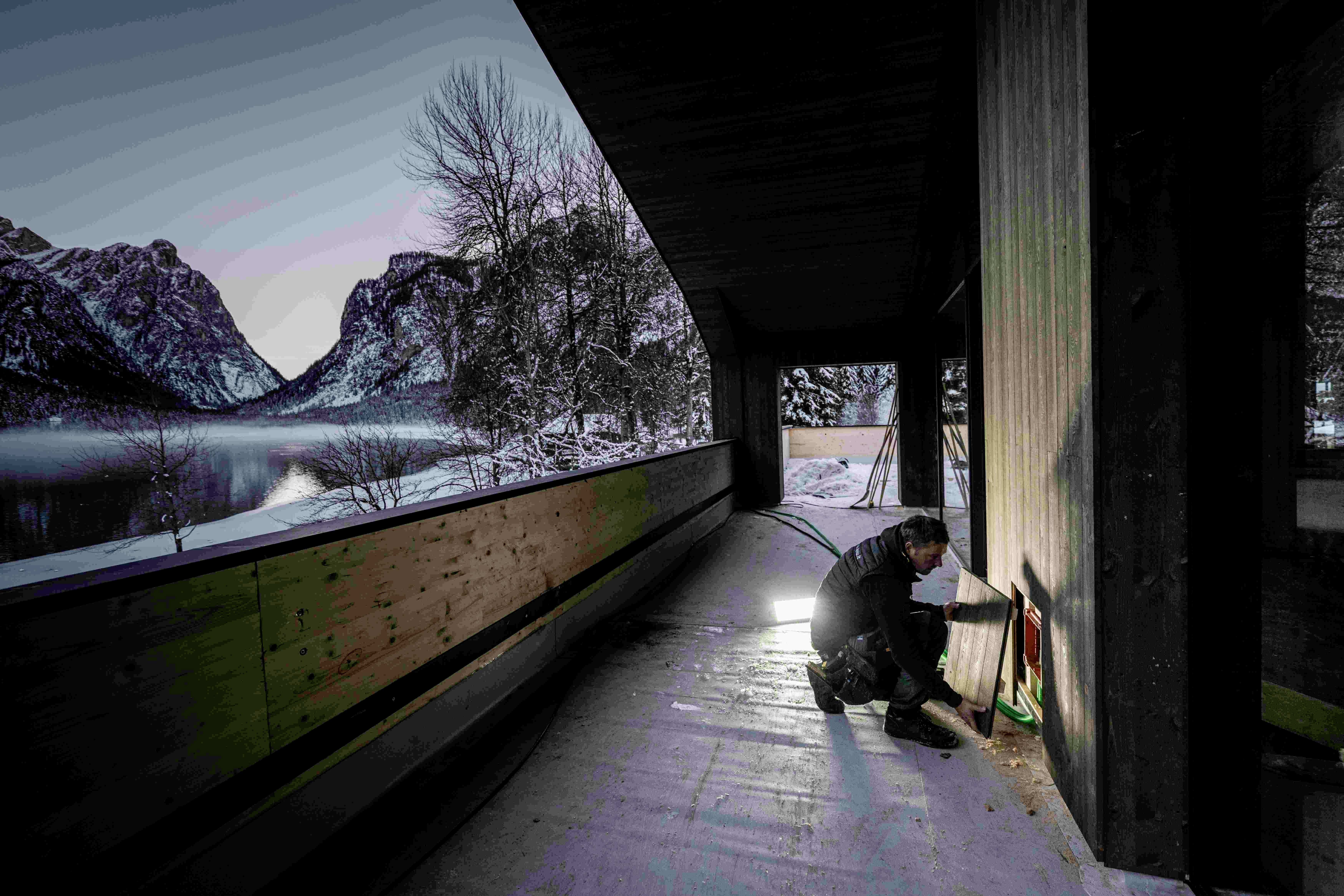 Ein Mensch reinigt eine Fläche im Freien mit Blick auf schneebedeckte Berge und einen See während der Dämmerung.
