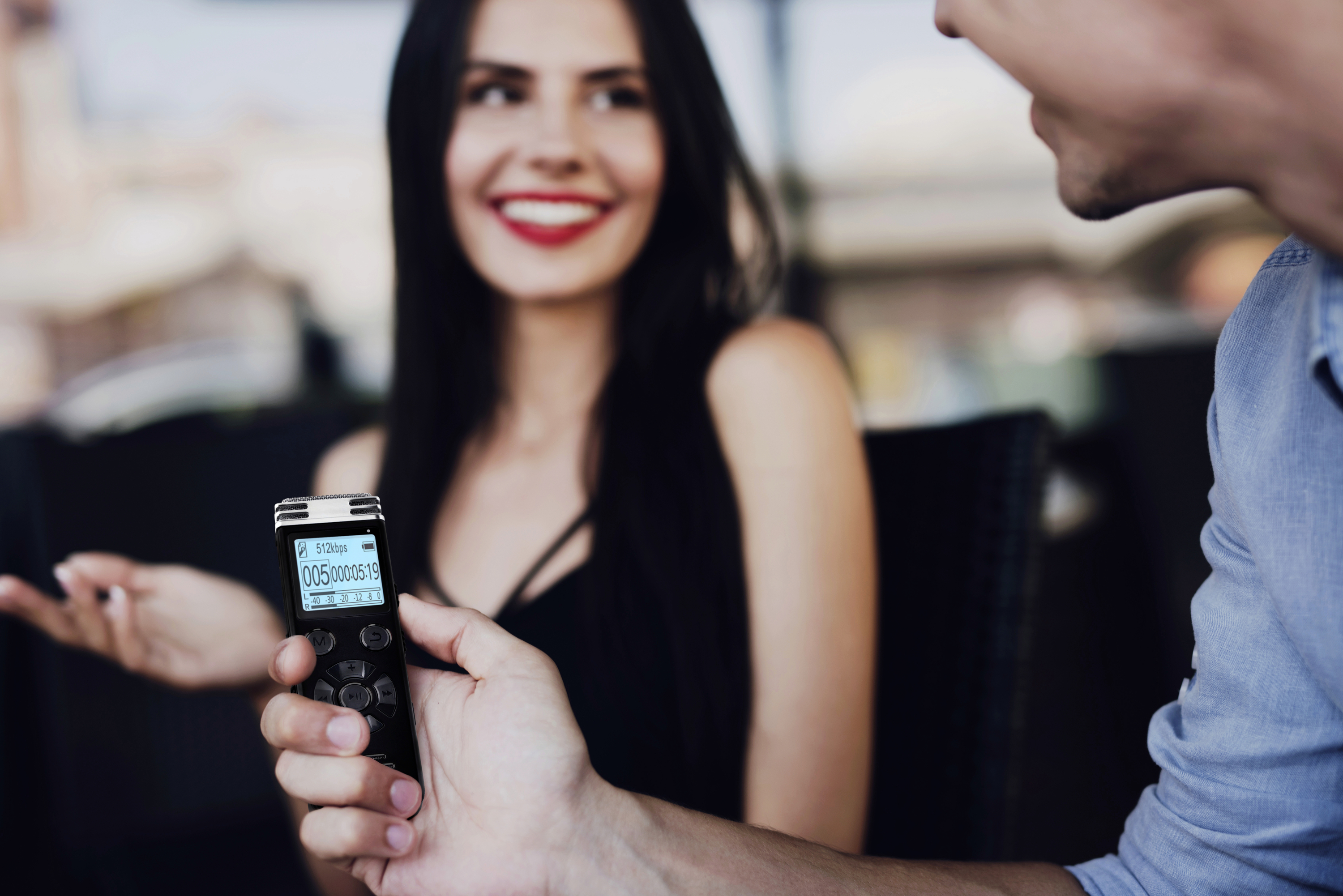 Eine Person hält ein Audiorecorder, während sie sich mit einer anderen Person unterhält. Die Unterhaltung scheint entspannt und freundlich.