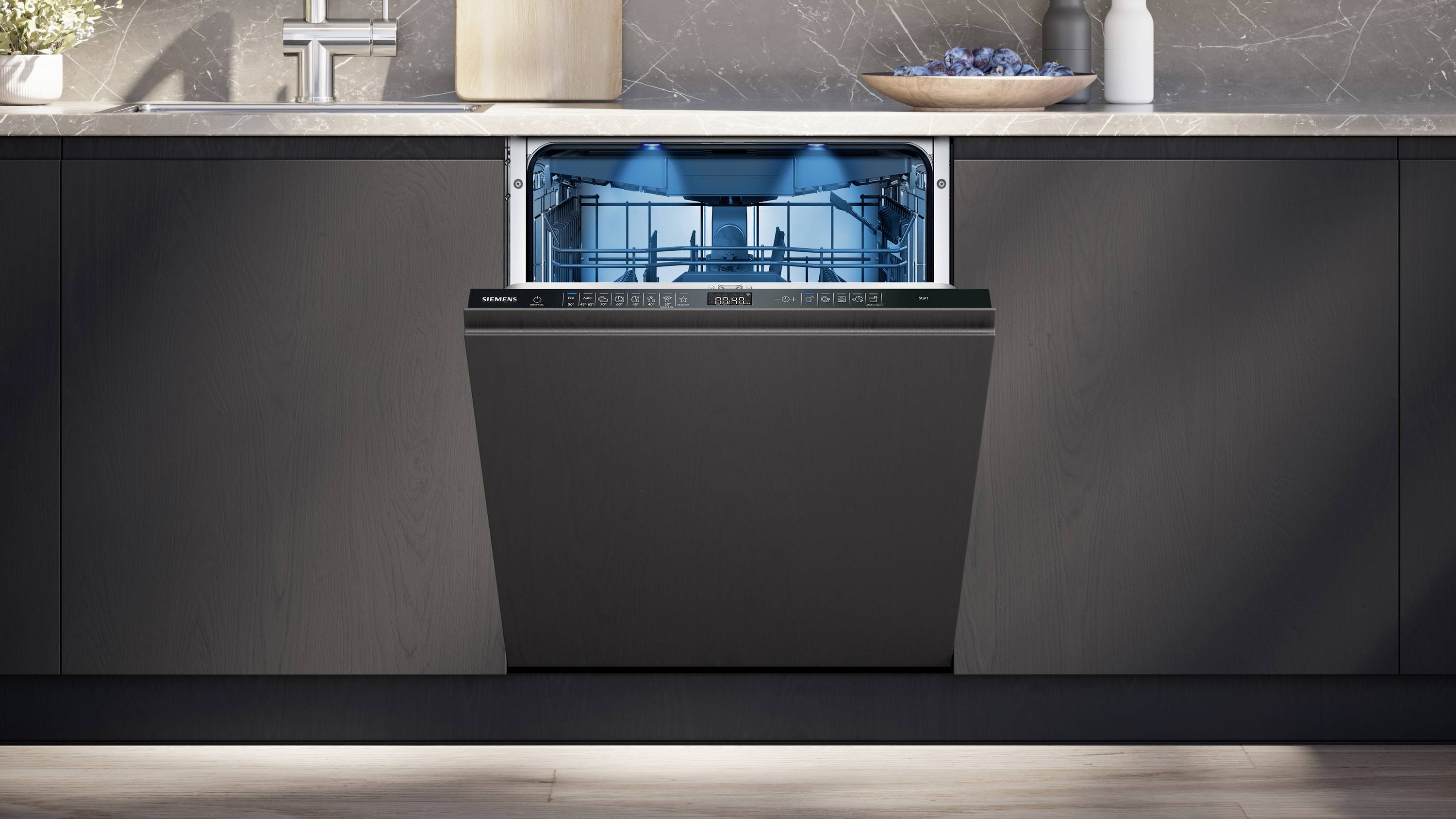 Eine moderne, offene Spülmaschine in einer Küche, die mit blauem Licht beleuchtet ist und teilweise mit Geschirr beladen ist.