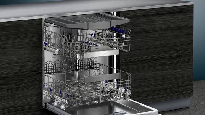 Ein Einbaugeschirrspüler von Siemens ist in eine Küchenzeile mit schwarzer Holzfront integriert. Die Tür steht komplett offen und alle Schubladen sind herausgezogen. Die Maschine verfügt über eine separate Besteckschublade und ist vollkommen leer.