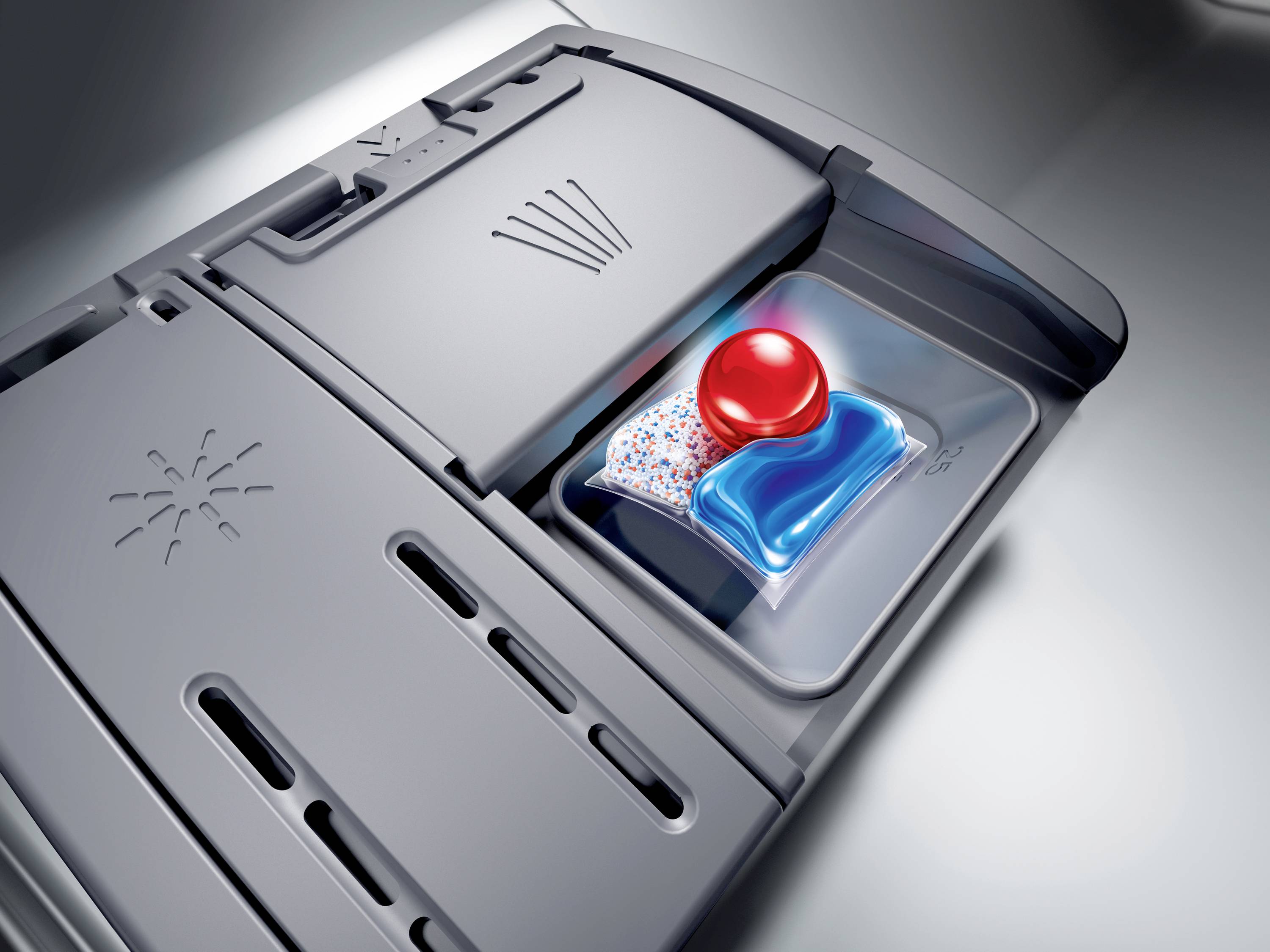 Ein geöffnetes Fach in einer Spülmaschine enthält eine bunte Geschirrspültablette mit rotem Ball für die Reinigung.