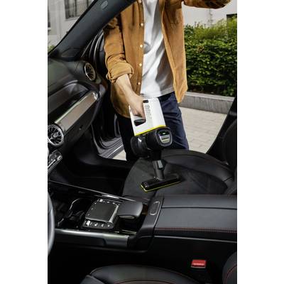 Person reinigt den Autositz mit einem Handstaubsauger. Der Innenraum des Autos ist modern mit Lederdetails.