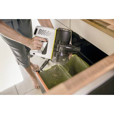Eine Person entleert den Inhalt eines kabellosen Staubsaugers in einen Mülleimer in einer Küche. Hände und Staubsauger sind sichtbar.