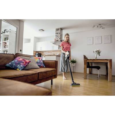 Frau in einem modernen, hellen Wohnzimmer staubsaugt den Holzfußboden. Im Hintergrund sind ein Holztisch, Stühle und eine Küche zu sehen.