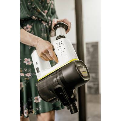 Person hält einen weißen und schwarzen kabellosen Staubsauger. Sie trägt ein grünes Kleid mit Blumenmuster.