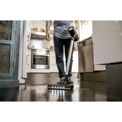Person reinigt dunklen Küchenboden mit einem staubsaugerähnlichen Gerät. Küche im Hintergrund; Fokus auf Reinigung.