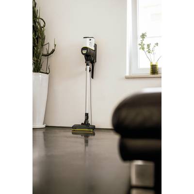 Kabelloser Staubsauger an einer weißen Wand gelehnt, neben einem großen Pflanzengefäß, in einem modernen, gut beleuchteten Raum.