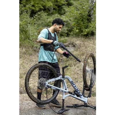 Ein Mann wäscht ein Mountainbike mit einem Hochdruckreiniger auf einem Weg im Wald.