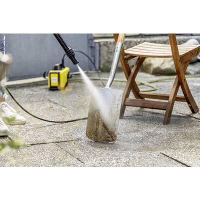 'Eine Person reinigt eine Schaufel mit einem Hochdruckreiniger auf einer Terrasse. Im Hintergrund steht ein Holzstuhl.'