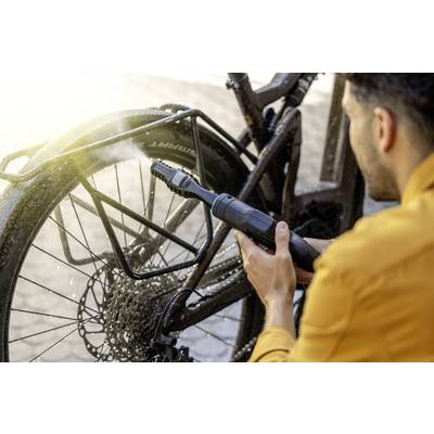 Eine Person reinigt ein Fahrrad mit einem Hochdruckreiniger, der Wasser auf das schmutzige Hinterrad sprüht.