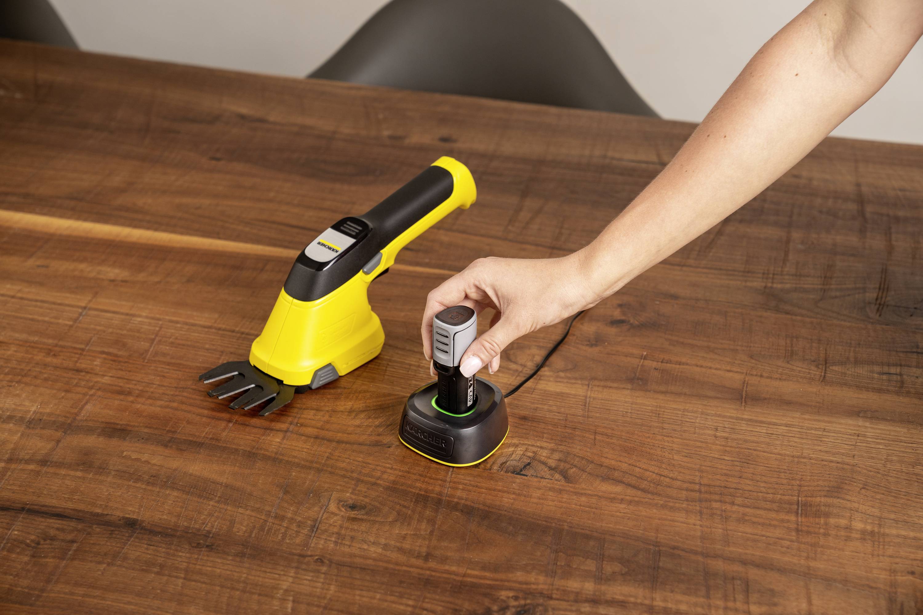 Eine Person platziert einen abnehmbaren Griff eines elektronischen Geräts in eine Ladeschale auf einem Holztisch.