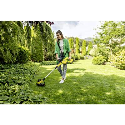 Eine Person mäht mit einem Trimmer den Rasen in einem gepflegten Garten, umgeben von Bäumen und Büschen an einem sonnigen Tag.