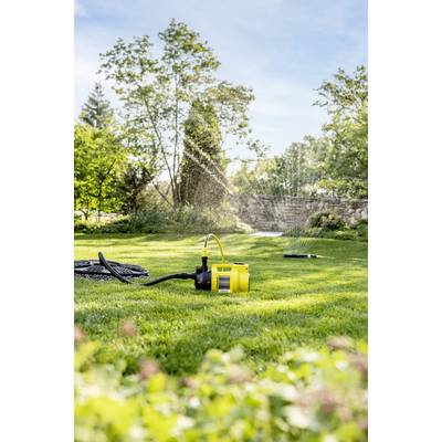 Ein gelber Gartensprenger bewässert Rasen in einem sonnigen Garten, umgeben von Bäumen und Sträuchern.