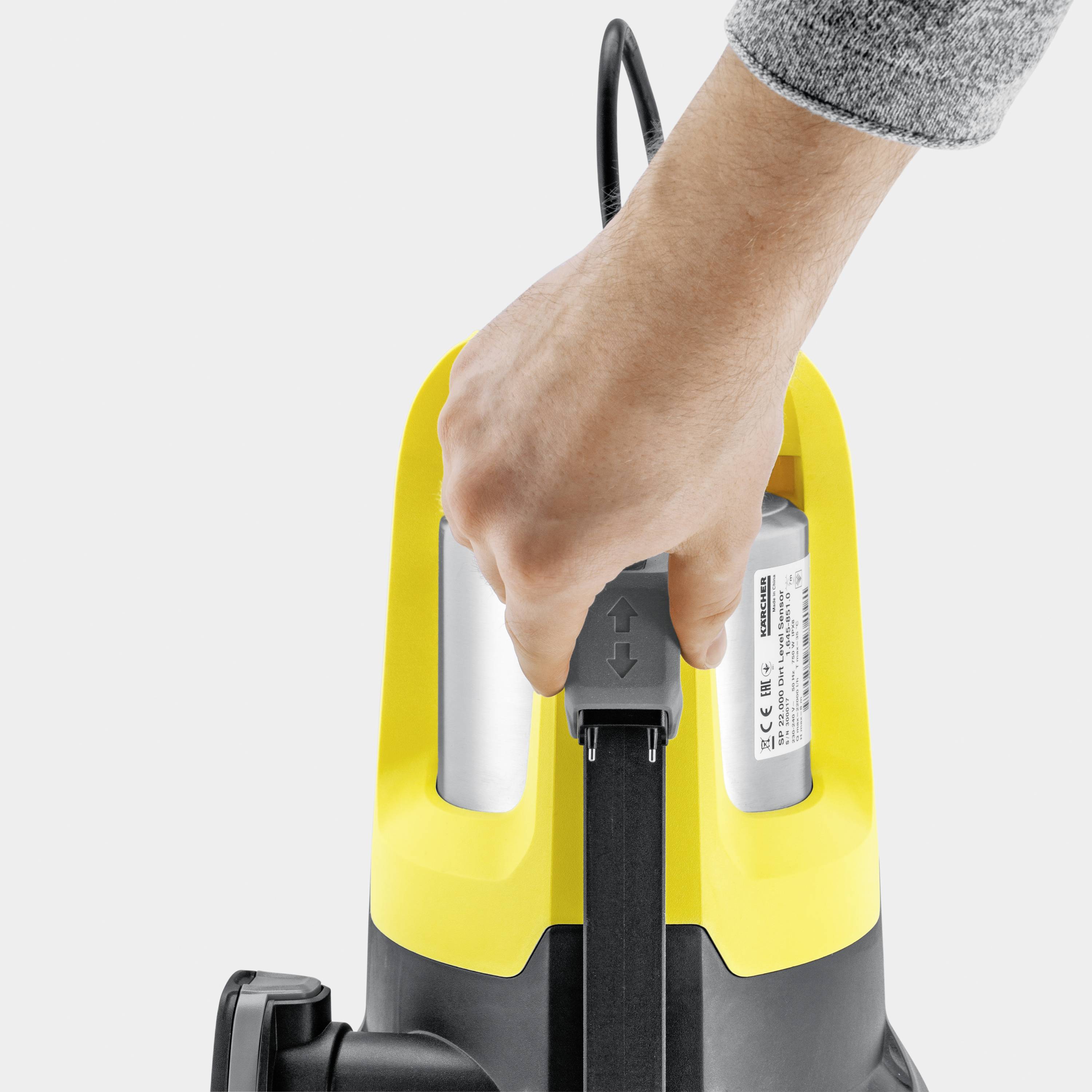 Ein gelber Hochdruckreiniger wird von einer Hand getragen. Die Hand greift an einem Tragegriff, was auf die Mobilität des Geräts hinweist.