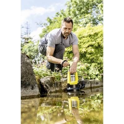 Ein Mann verwendet eine gelbe Tauchpumpe, um Wasser aus einem kleinen Teich in einem Garten abzulassen. Umgeben von Pflanzen und Bäumen.