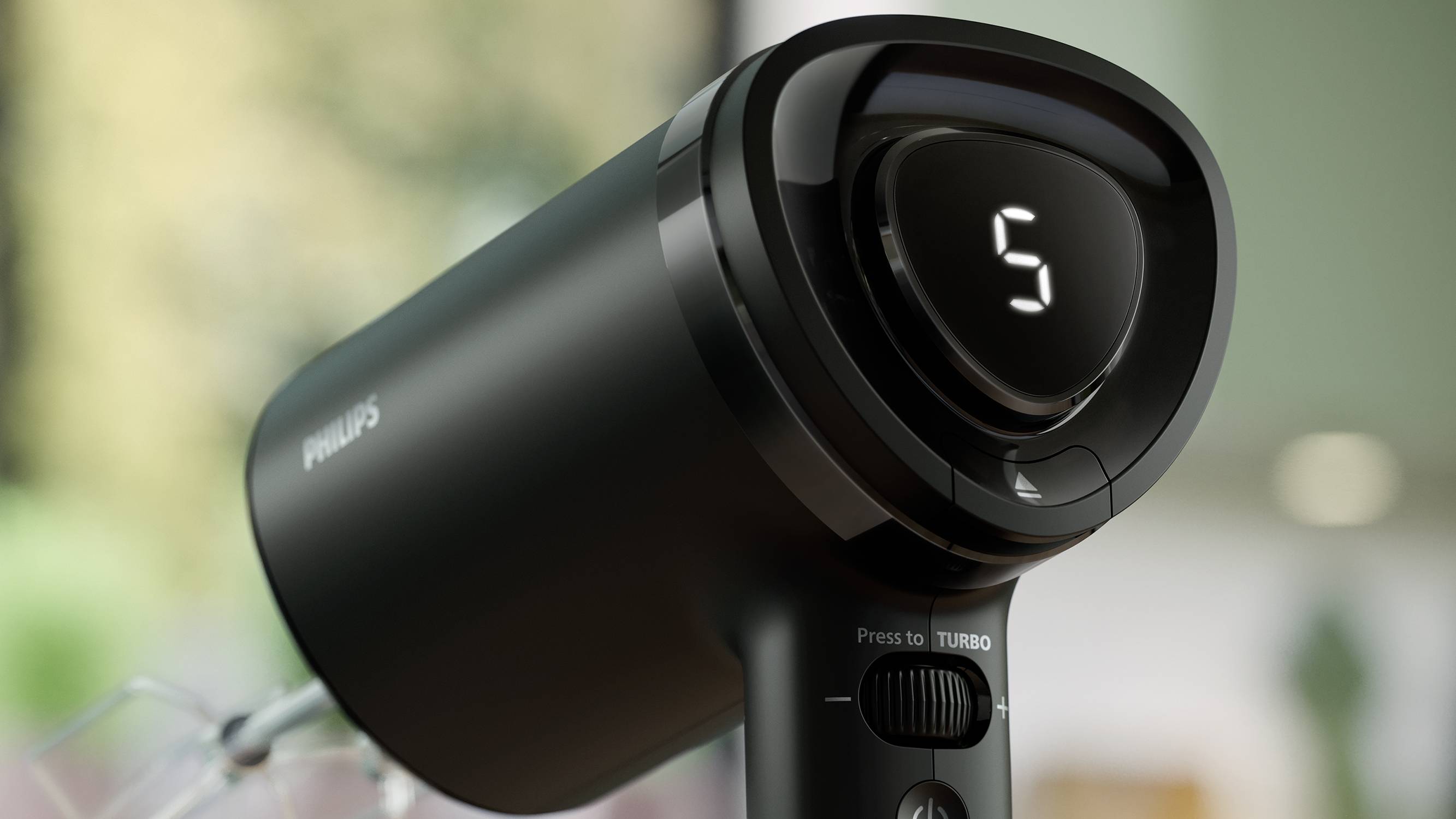 Schwarzer Haartrockner mit Digitalanzeige '5'. Er steht auf einem Tisch, umgeben von einer verschwommenen, grünen Umgebung im Hintergrund.