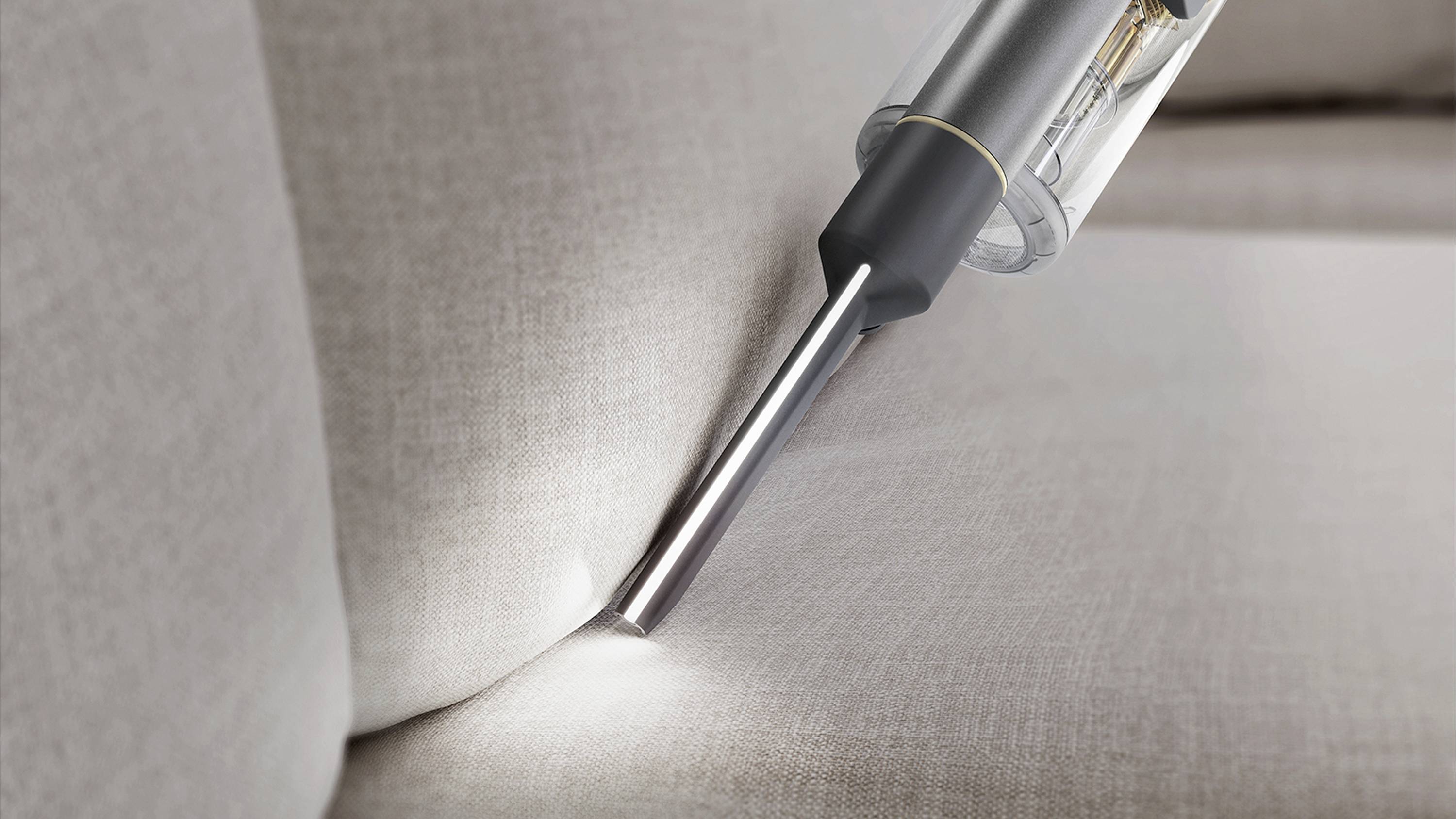 Ein Staubsauger mit schmaler Düse saugt Schmutz aus einer Sofaritze.