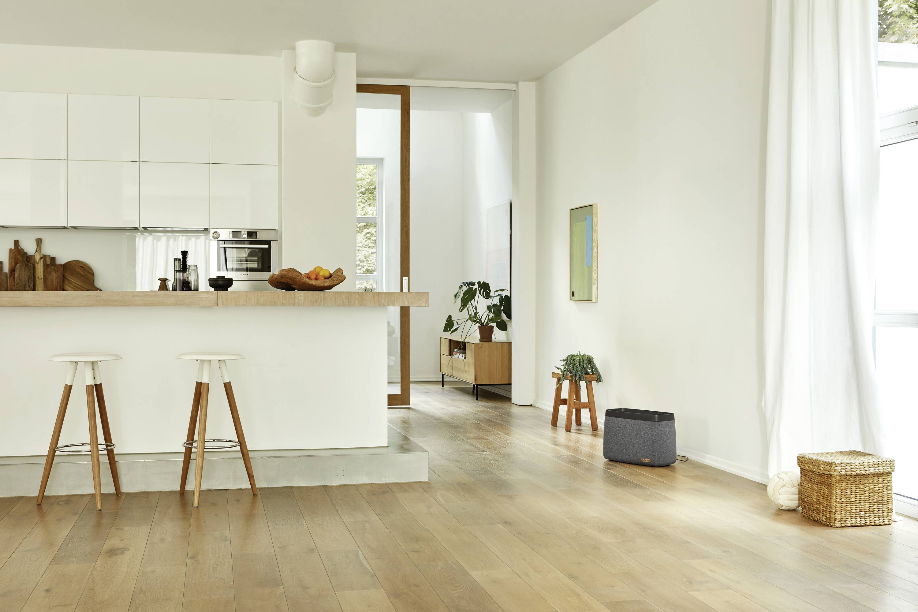 Moderne, minimalistische Küche mit weißem Farbton. Zwei Barhocker stehen an der Theke. Helles Holzparkett und große Fenster.