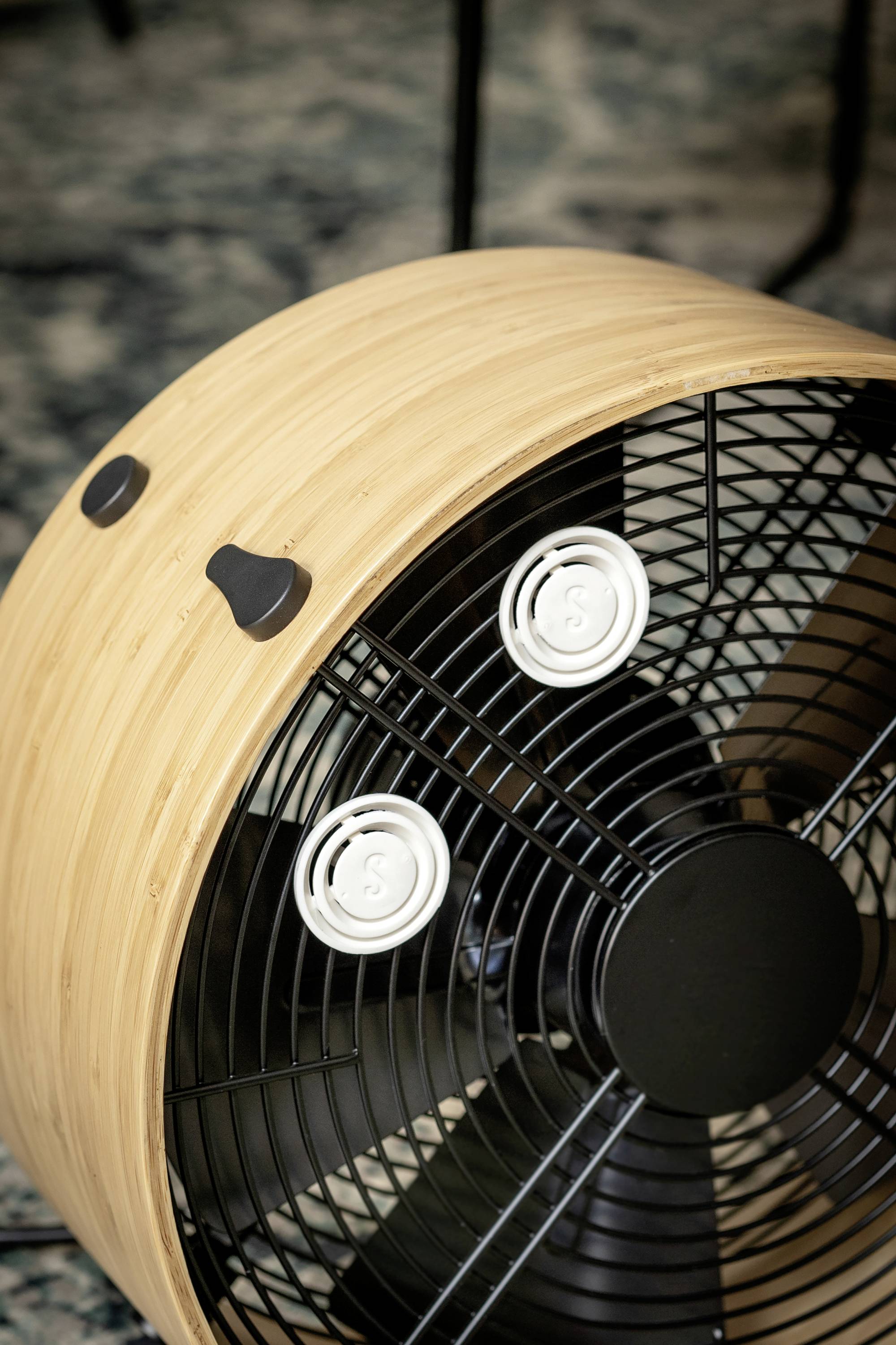Ein Ventilator mit Holzeffekt-Gehäuse, drei schwarzen Rotorblättern und zwei einstellbaren Drehknöpfen für Geschwindigkeit und Neigung.