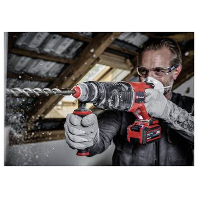 Eine Person mit Sicherheitsbrille und Handschuhen benutzt eine rote und schwarze Bohrmaschine, um ein Loch in einen Holzbalken in einem Raum unter Renovierung zu bohren.