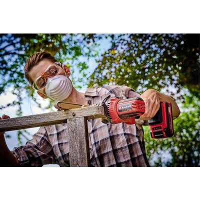 Ein Mann trägt Schutzbrille und Maske, verwendet eine elektrische Säge, um Holz im Freien zu bearbeiten, umgeben von Bäumen.