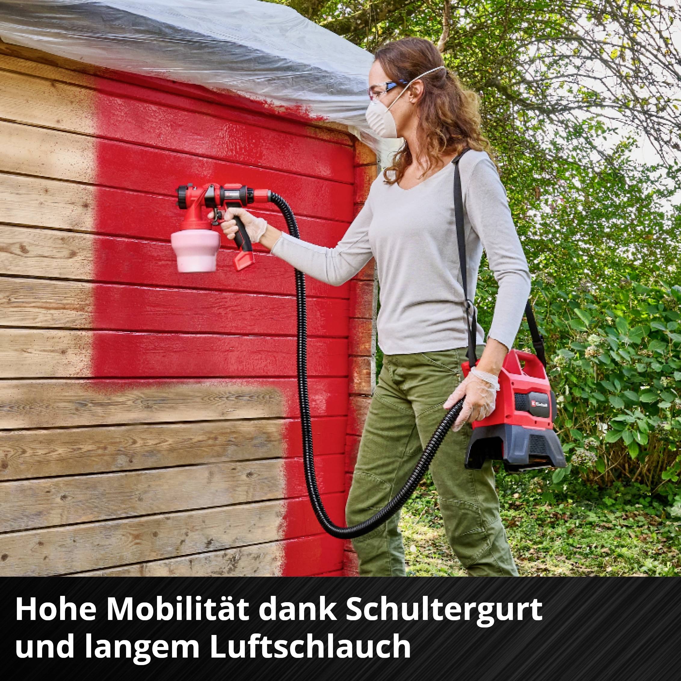 Eine Person sprüht mit einem Farbsprühgerät eine Holzwand rot an. Text: 'Hohe Mobilität dank Schultergurt und langem Luftschlauch'.