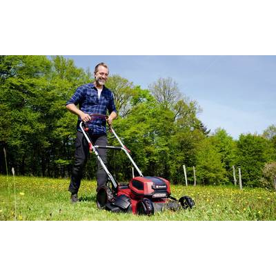 Ein Mann mäht Rasen mit einem elektrischen Rasenmäher auf einer Wiese an einem sonnigen Tag, umgeben von Bäumen.