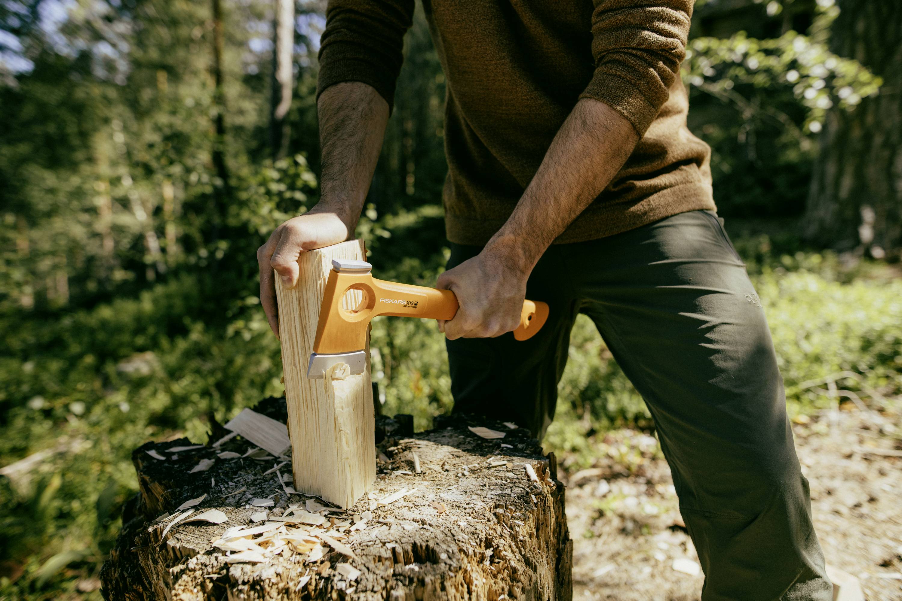Eine Person spaltet draußen in einem Waldstück ein Stück Holz mit einer Axt.