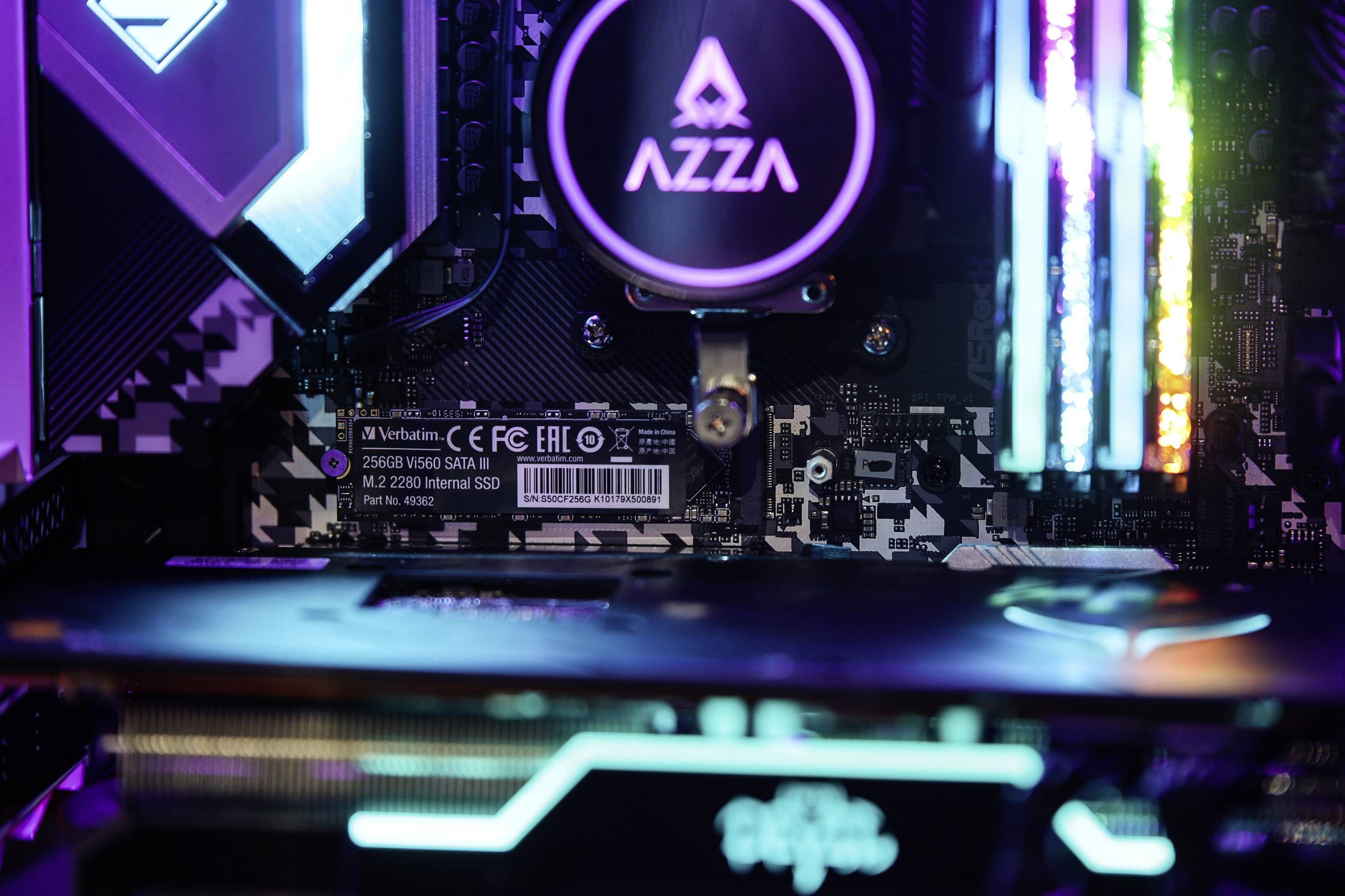 Nahaufnahme eines beleuchteten Computer-Motherboards mit sichtbaren Komponenten wie einem AZZA-Kühler und RGB-beleuchteten Details.