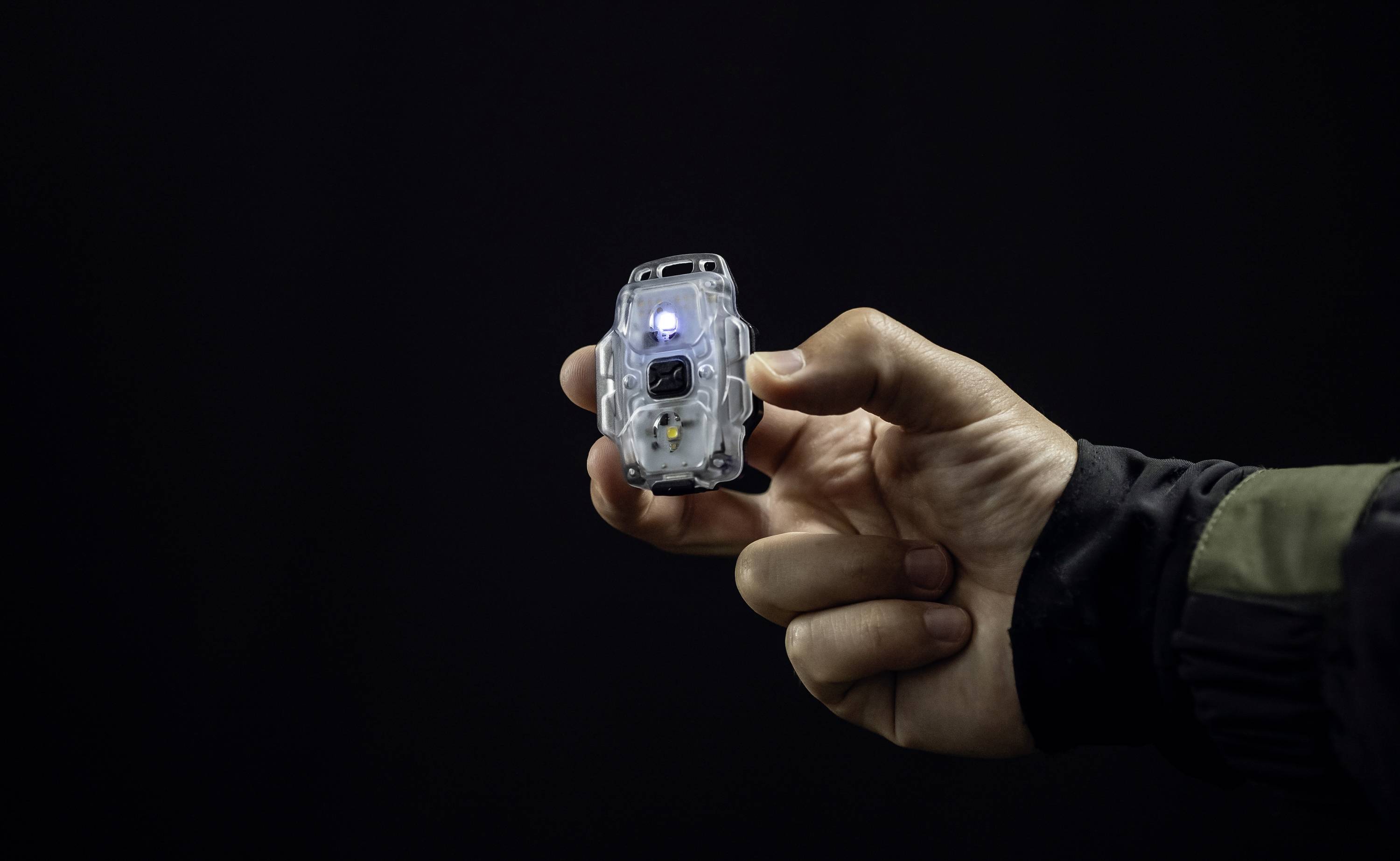 Eine Hand hält ein kleines, leuchtendes elektronisches Gerät in einem dunklen Hintergrund.