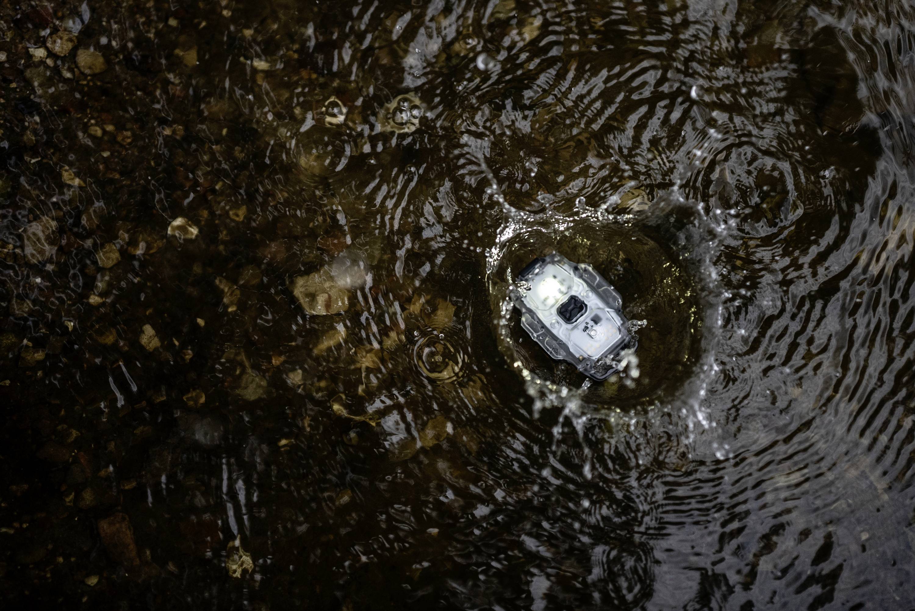 Ein kleines ferngesteuertes Auto fährt durch eine Pfütze, spritzt Wasser auf und erzeugt Wellen im Wasser.