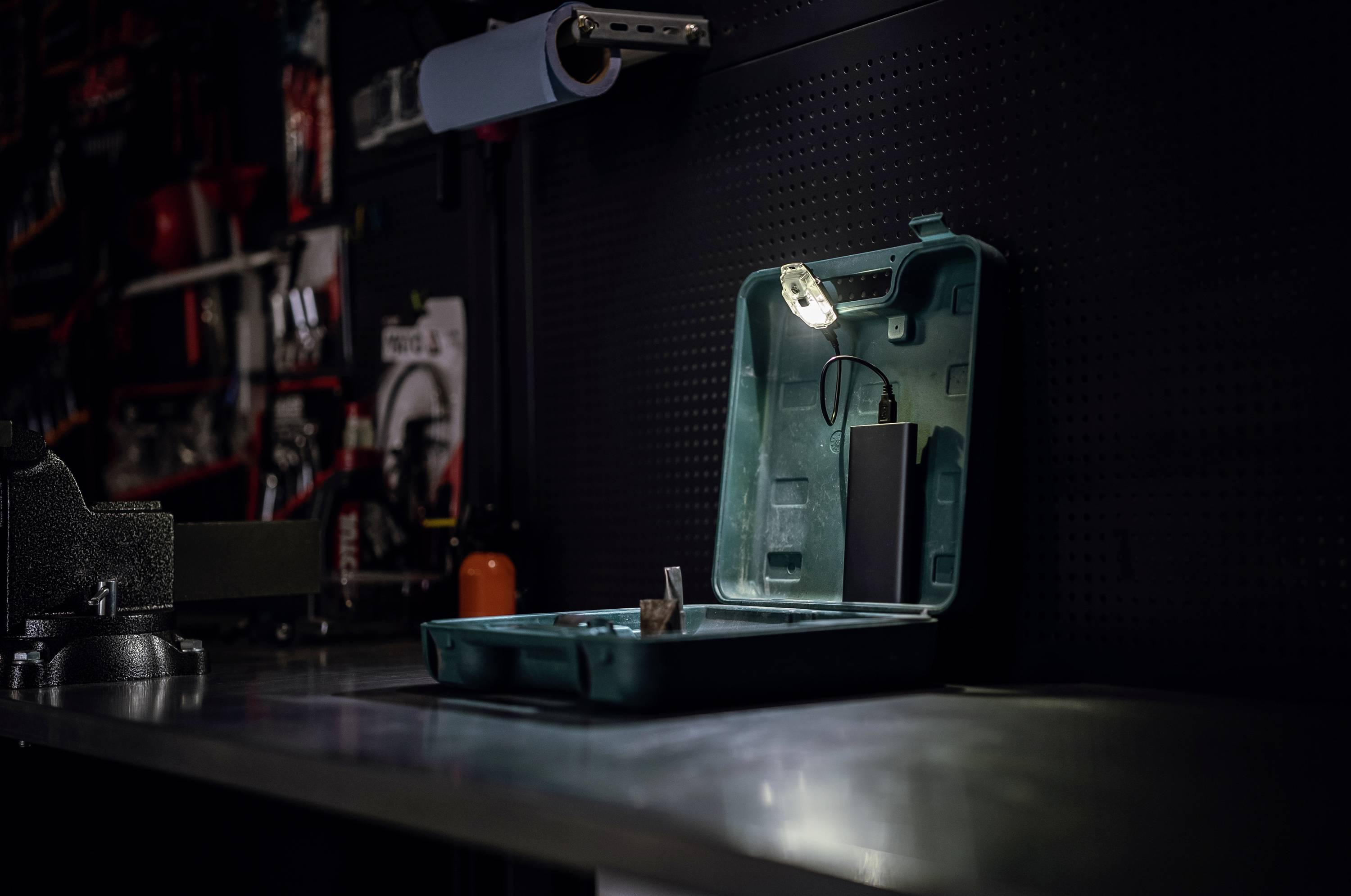 Ein offener Werkzeugkoffer mit einer Lampe steht auf einer Werkbank in einer Werkstatt. Im Hintergrund sind verschiedene Werkzeuge zu sehen.