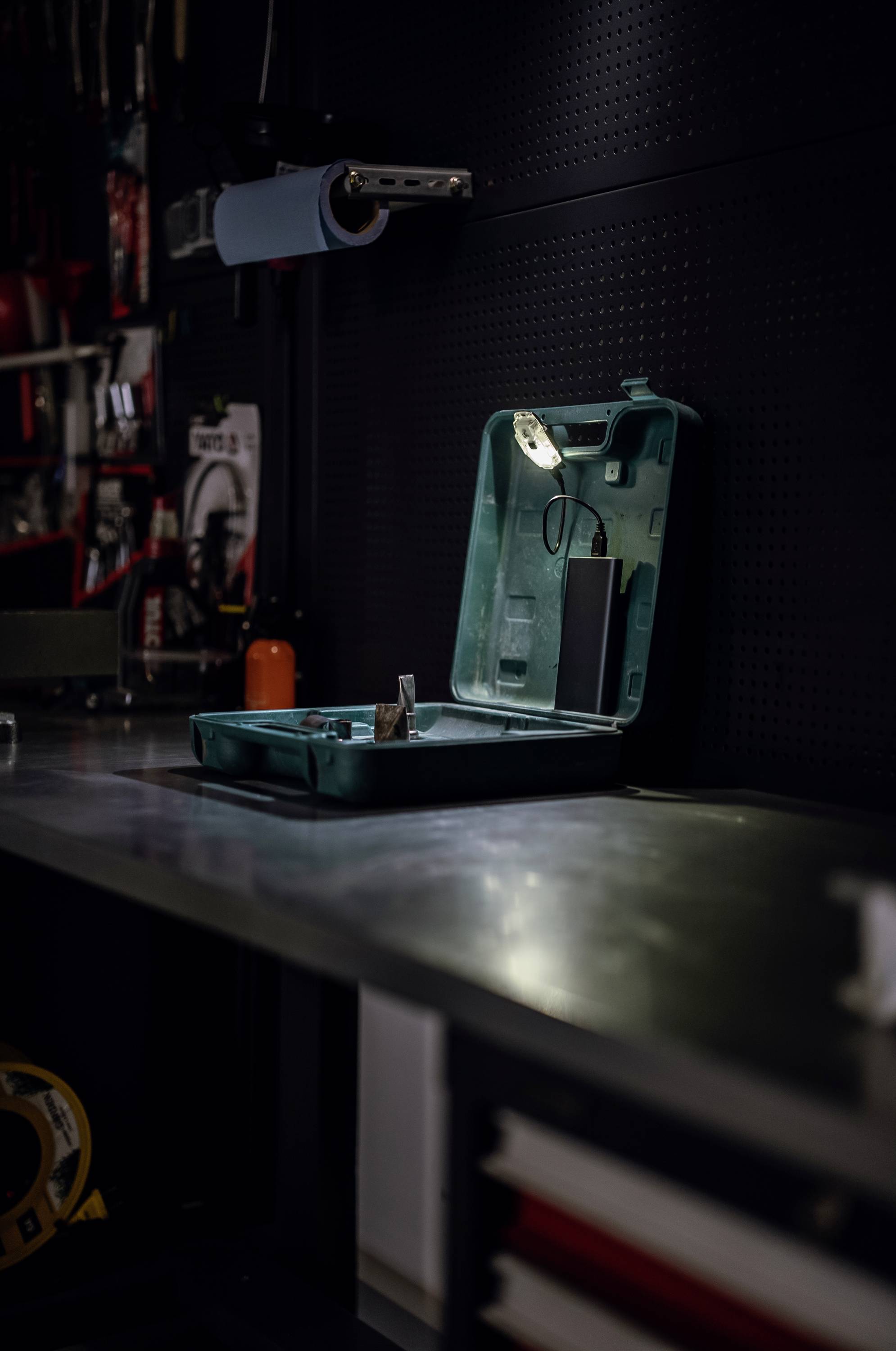 Geöffneter grüner Werkzeugkoffer auf einem Werkbank in einer Werkstatt, umgeben von Werkzeugen und Geräten im Hintergrund.