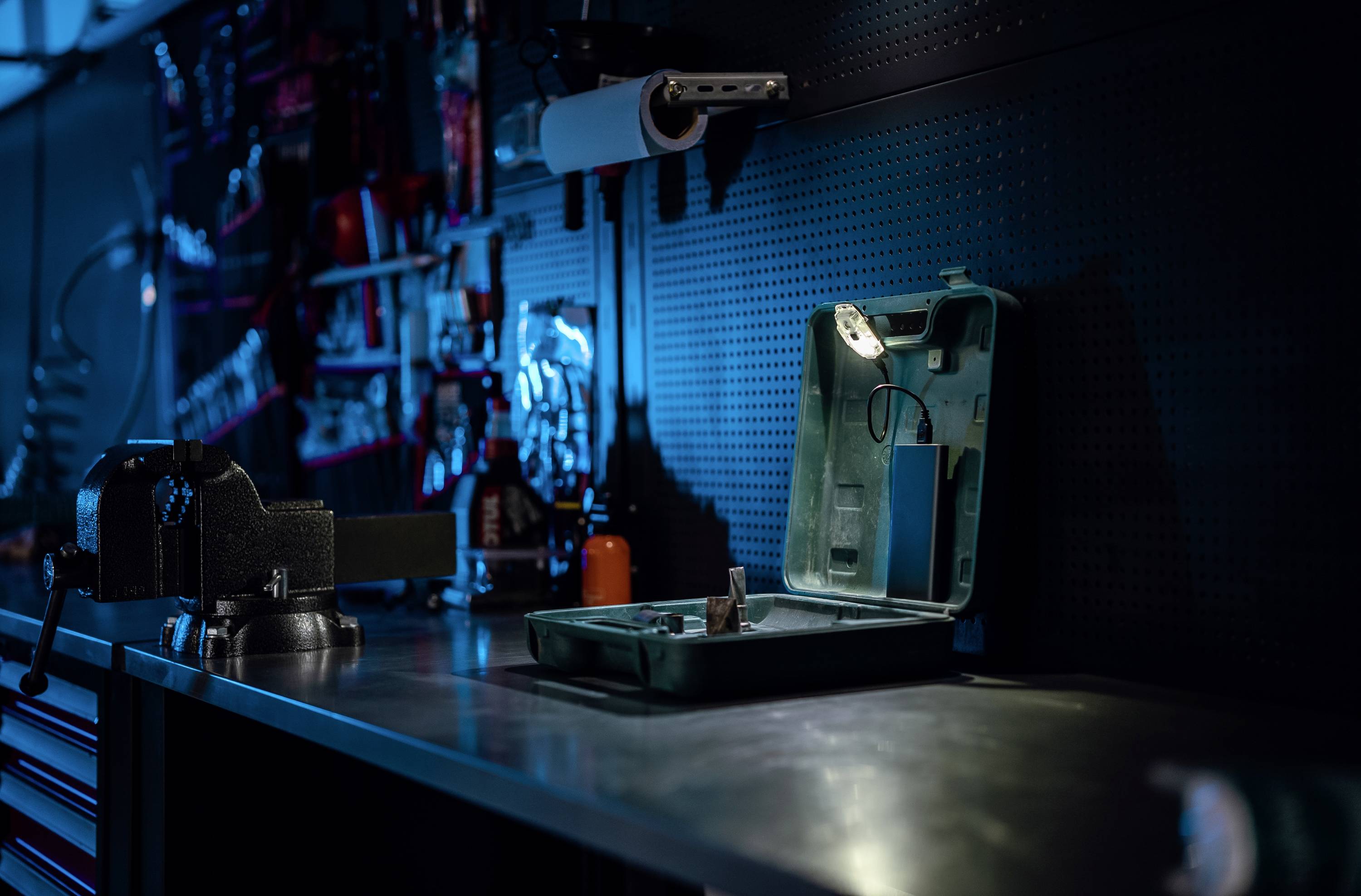 Werkbank mit Werkzeugkasten und Lampe; verschiedene Werkzeuge an der Wand.