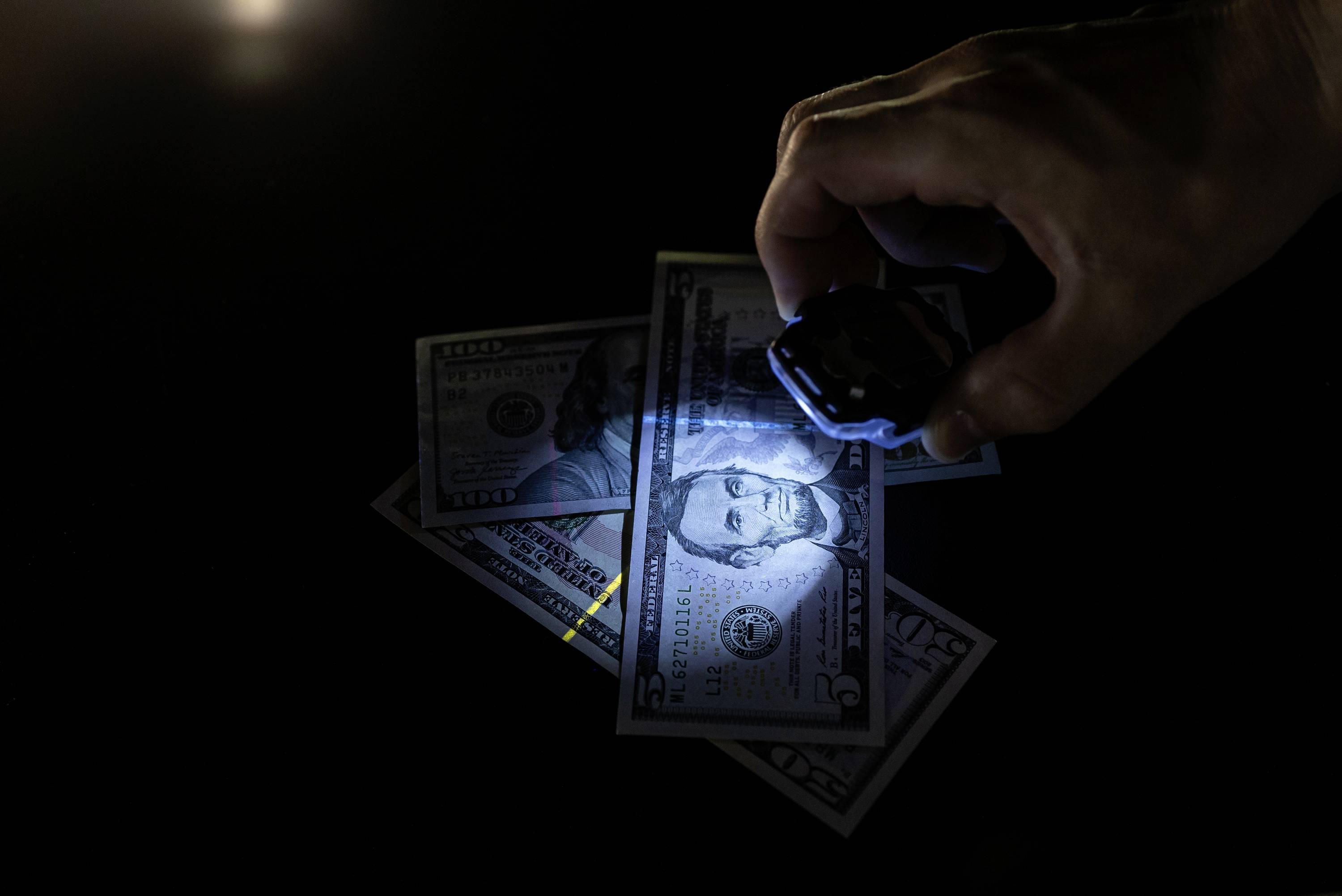 Eine Hand beleuchtet mit UV-Licht drei Dollar-Scheine, um ihre Echtheit zu überprüfen.