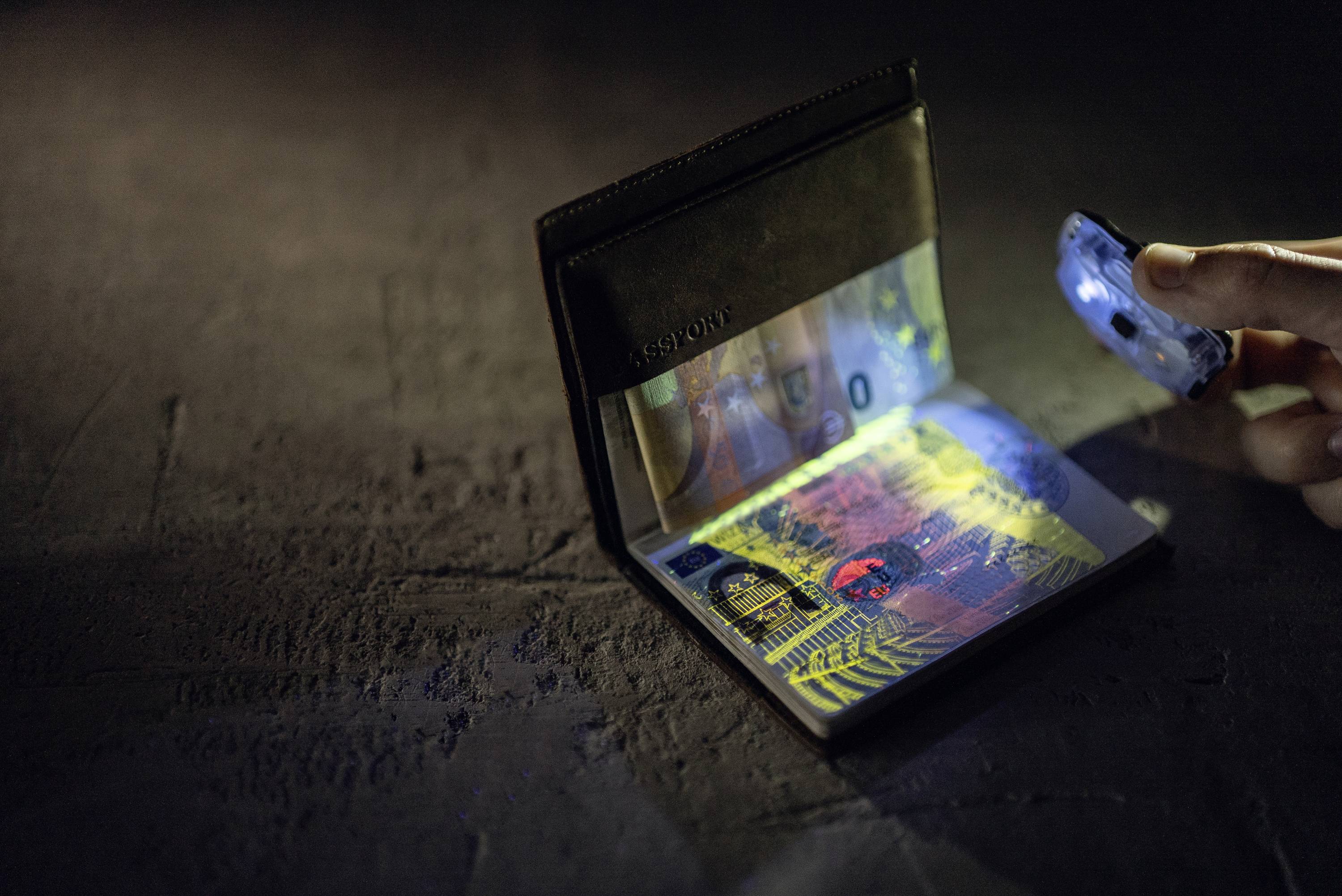 Eine Hand leuchtet mit einer UV-Lampe auf einen geöffneten Reisepass, um die Sicherheitsmerkmale zu prüfen.