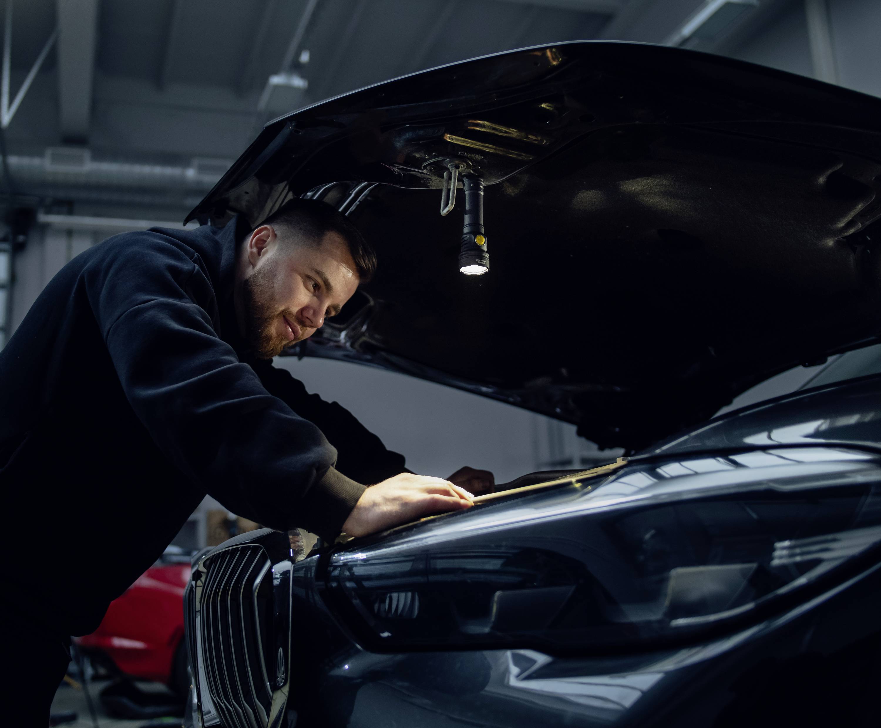Ein Mechaniker inspiziert den Motorraum eines geöffneten Autos in einer Werkstatt und überprüft die Fahrzeugkomponenten.