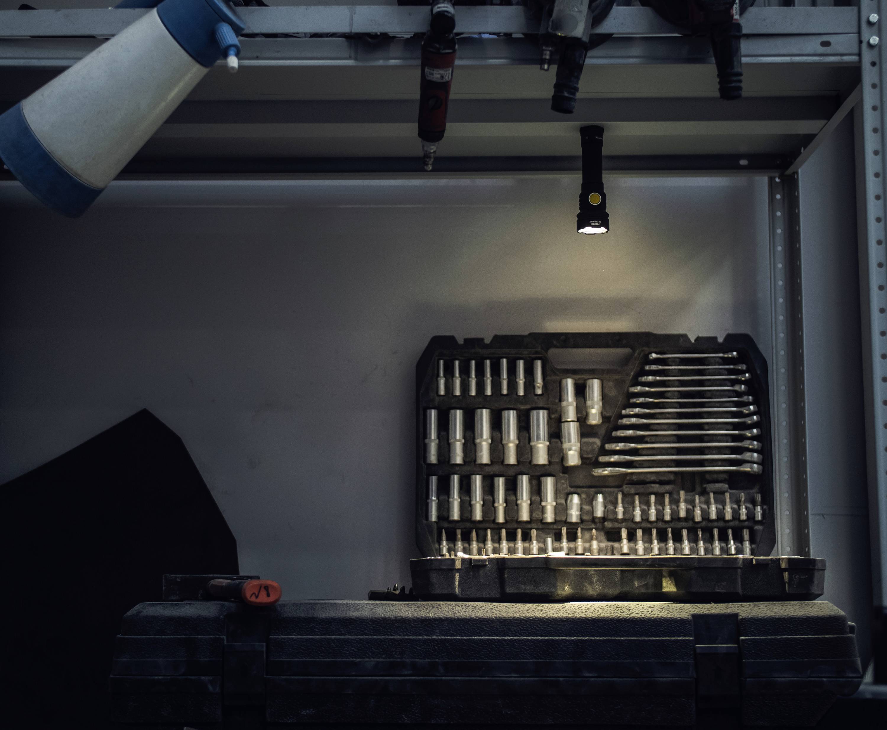 Werkstatt mit Werkzeugkoffer, der verschiedene Stecknüsse und Schraubenschlüssel zeigt. Eine Lampe beleuchtet den Raum.