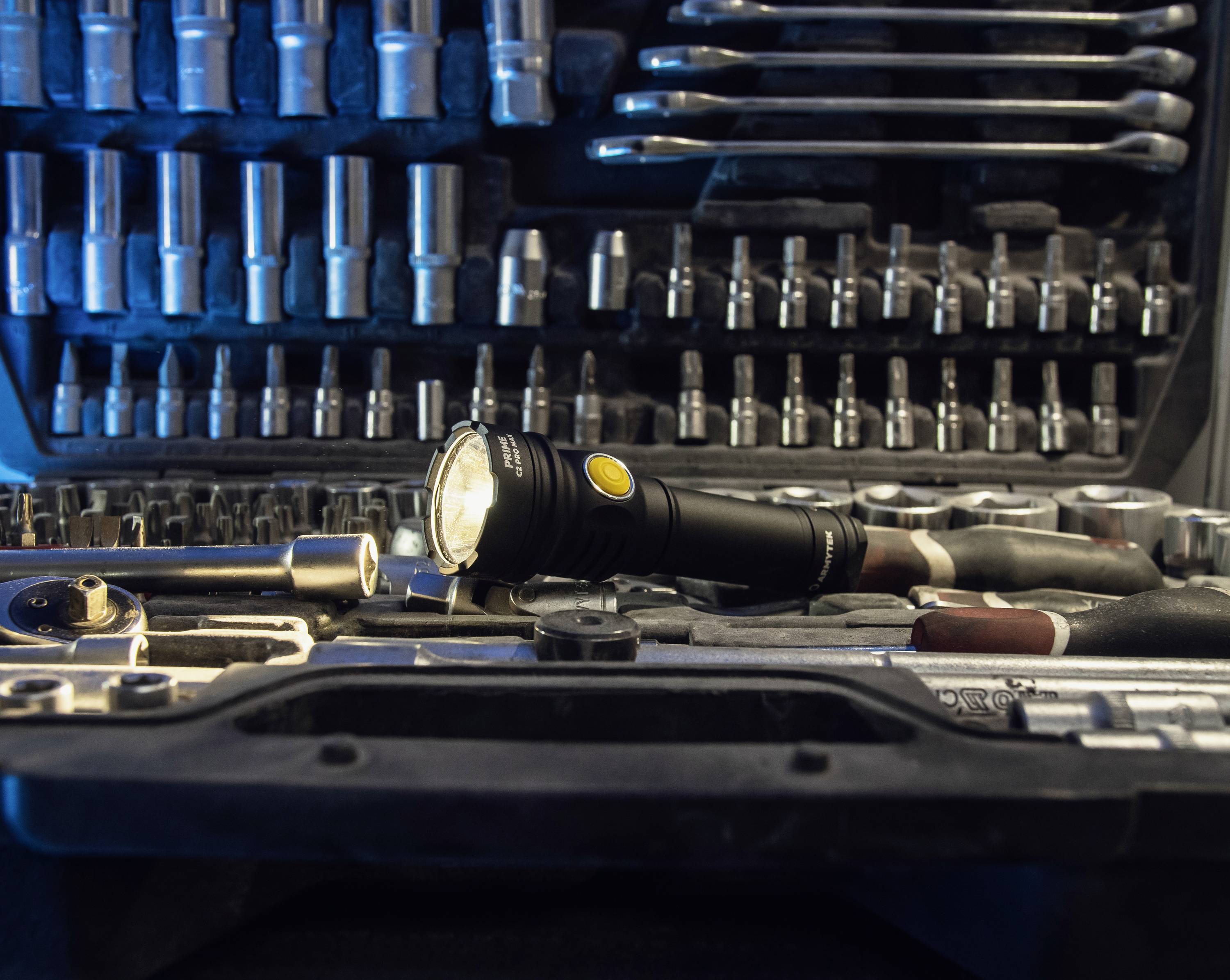 Ein geöffneter Werkzeugkoffer mit Steckschlüsseln und Schraubenschlüsseln. Eine Taschenlampe liegt in der Mitte, eingeschaltet.