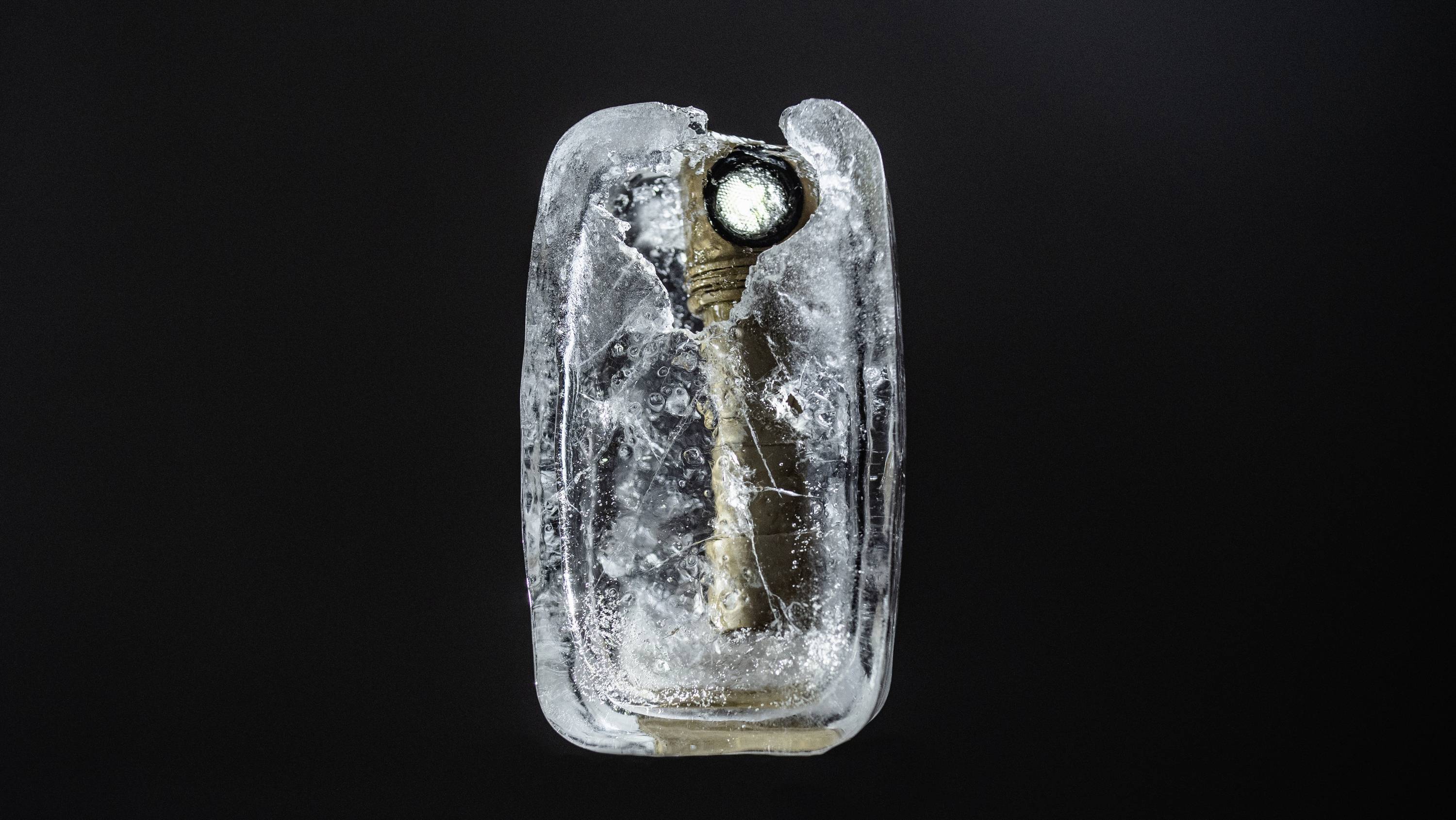 Gefrorene antike Taschenlampe in Eisblock, schwebend vor schwarzem Hintergrund.