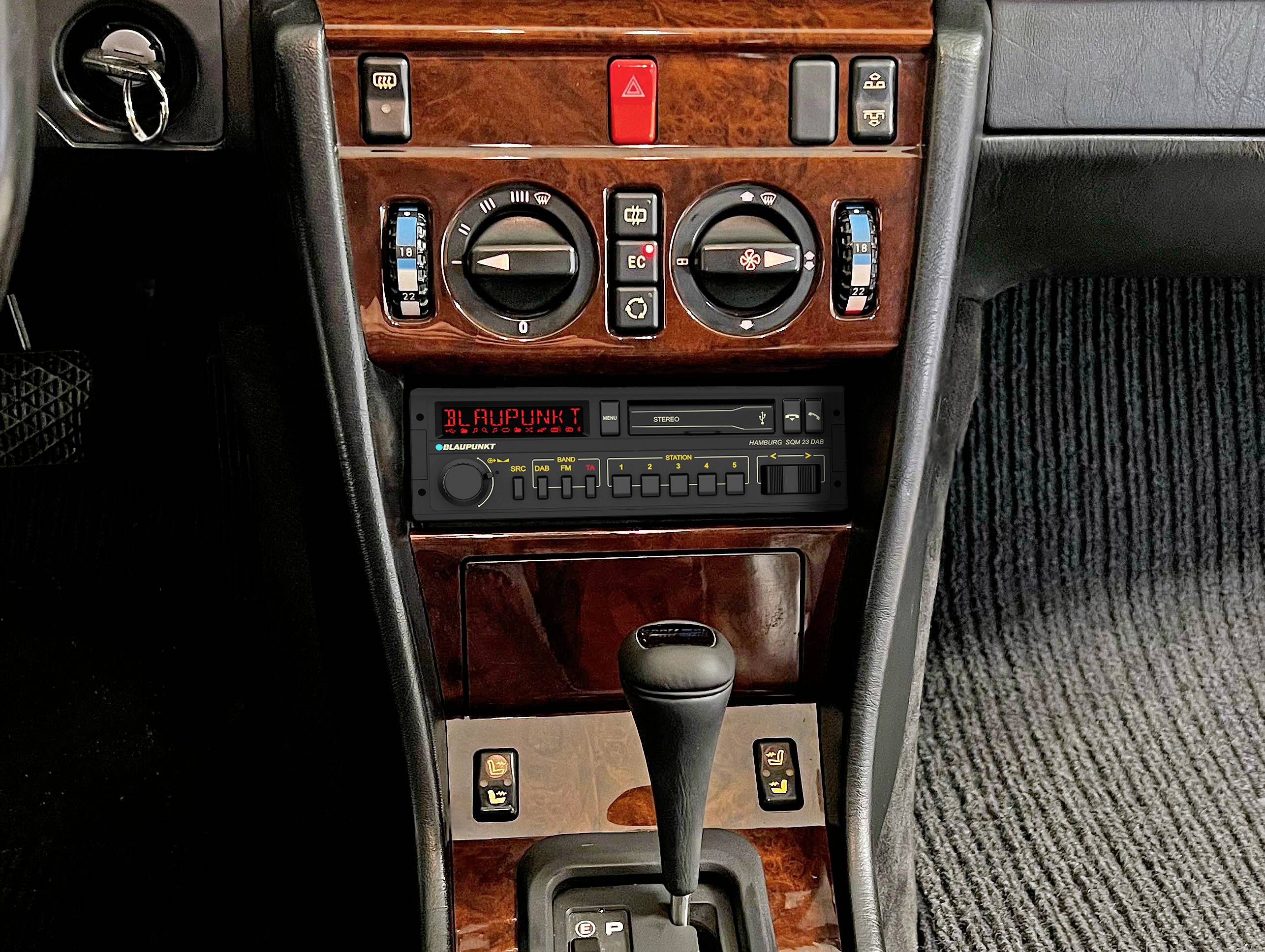 Autoradio und Klimawähler in der Mittelkonsole eines Autos mit holzgetäferten Oberflächen und Automatikgetriebeschaltung.