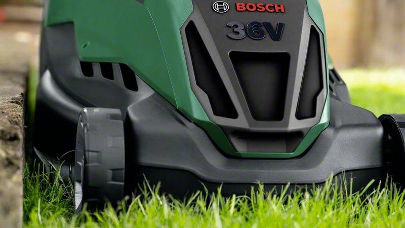 Ein grüner Rasenmäher mit der Aufschrift 'Bosch 36V' mäht grasbewachsene Fläche. Scharfkantiges, modernes Design betont Funktionalität.