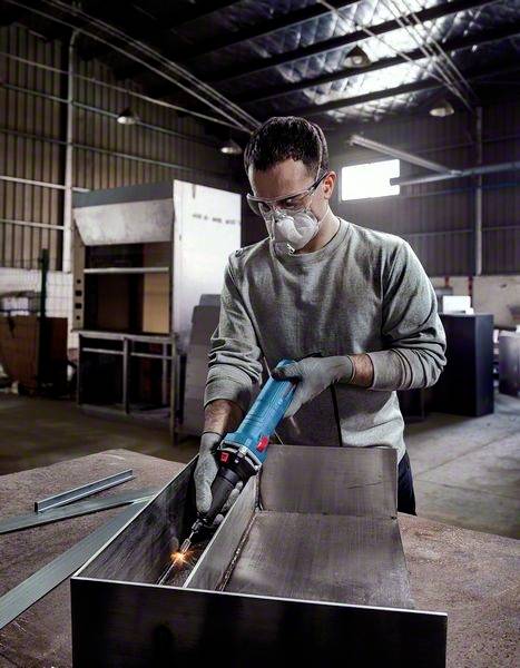 Ein Mann trägt Schutzkleidung und schweißt in einer Werkstatt an einem Metallstück. Er verwendet ein elektrisches Schweißgerät.