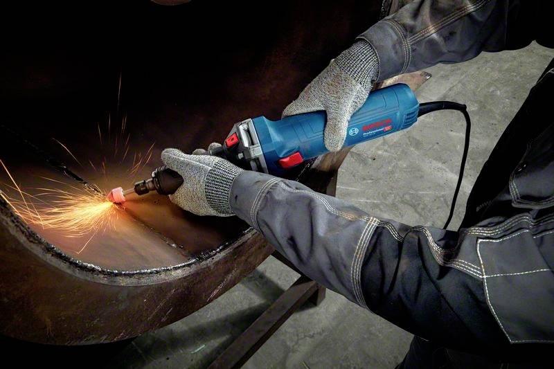 Eine Person in Schutzkleidung schleift mit einem Elektrowerkzeug Metall, Funken fliegen vom Kontaktpunkt.