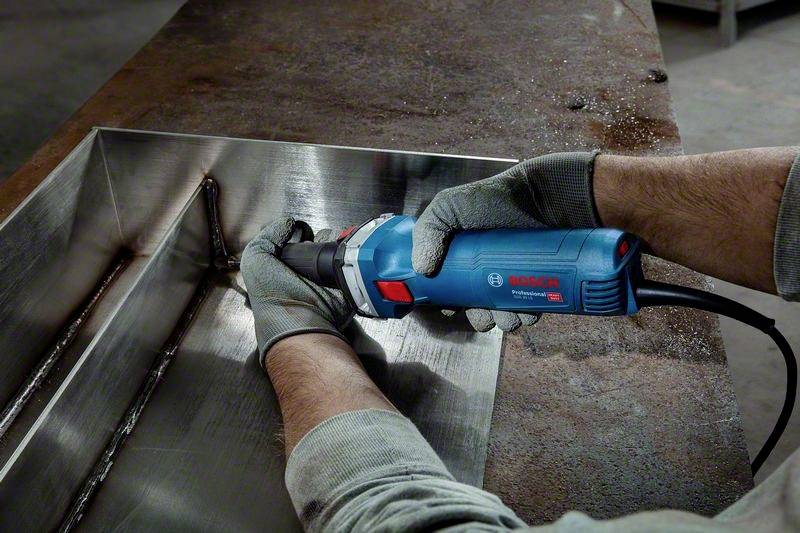 Eine Person benutzt ein blaues Elektrowerkzeug, um Schweißnähte auf einem Metallstück abzuschleifen. Sie trägt graue Schutzhandschuhe.
