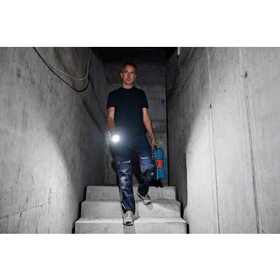 Eine Person steigt mit einer Taschenlampe und einem Werkzeugkoffer eine Betontreppe hinunter, vermutlich in einem Keller.