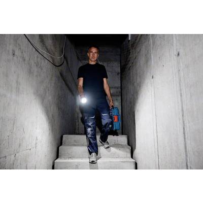 Eine Person geht eine Betonstiege hinab. Sie trägt eine Taschenlampe und eine Werkzeugkiste. Die Umgebung wirkt dunkel und industriell.