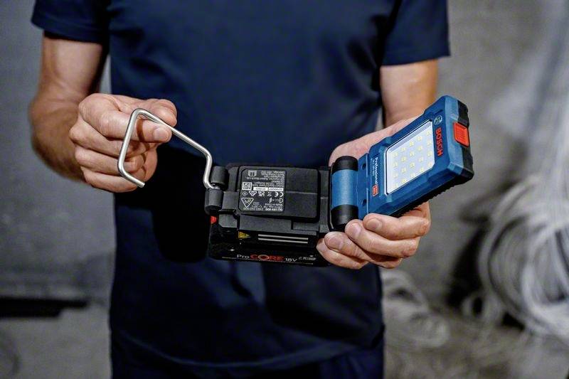 Person hält ein tragbares Arbeitsscheinwerferlicht, zeigt Rückseite mit Lade- und Batterieinformationen.