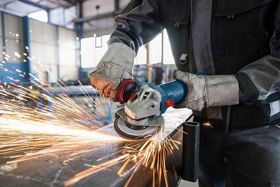 Ein Arbeiter in Schutzkleidung schleift Metall mit einem Winkelschleifer, Funken sprühen.